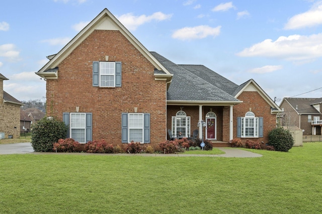 traditional-style house featuring a shingled roof, a front yard, and brick siding