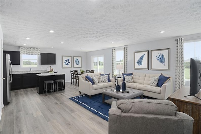 living room featuring light wood finished floors, baseboards, a textured ceiling, and recessed lighting