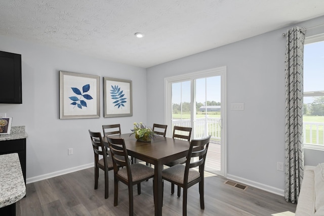 dining area featuring dark wood-style flooring, visible vents, a textured ceiling, and baseboards