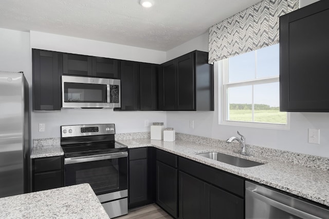 kitchen with dark cabinetry, appliances with stainless steel finishes, light stone counters, and a sink