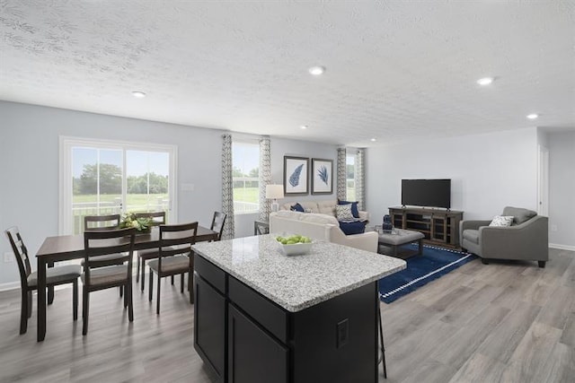 kitchen with open floor plan, dark cabinetry, a kitchen island, and light wood-style flooring