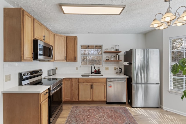 kitchen featuring stainless steel appliances, a sink, hanging light fixtures, light countertops, and a wealth of natural light