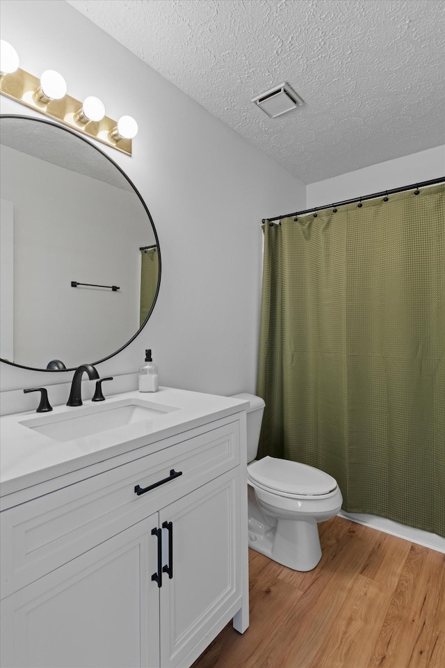 full bath with visible vents, toilet, vanity, a textured ceiling, and wood finished floors