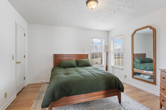 bedroom featuring baseboards, a textured ceiling, and light wood finished floors