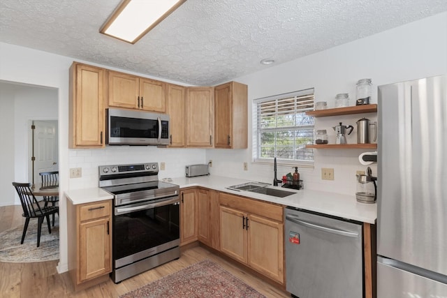 kitchen with stainless steel appliances, light countertops, a sink, and light wood-style flooring