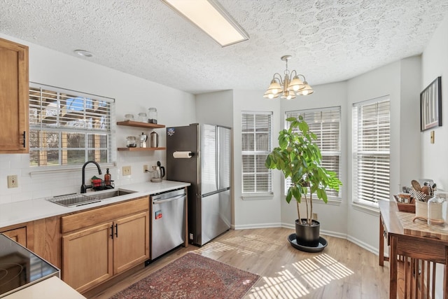 kitchen with a sink, hanging light fixtures, appliances with stainless steel finishes, and light countertops