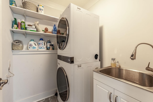 clothes washing area featuring a sink, cabinet space, stacked washer / drying machine, and baseboards