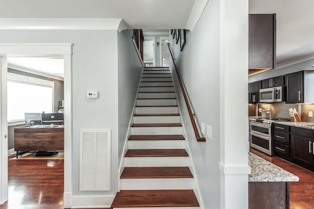 stairway with baseboards, ornamental molding, visible vents, and wood finished floors