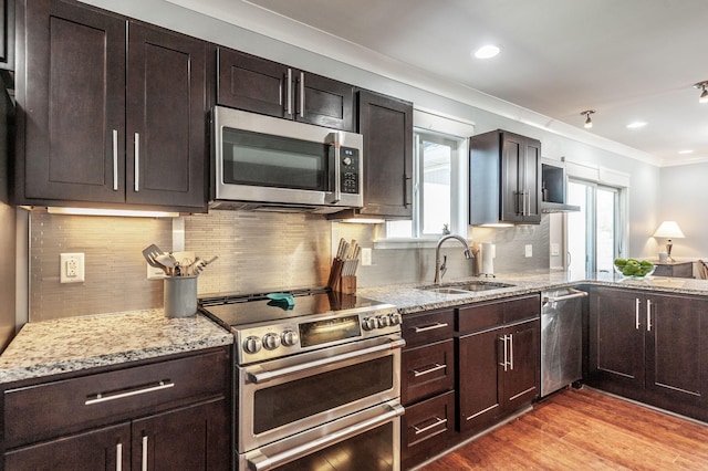 kitchen with ornamental molding, stainless steel appliances, a sink, light wood-type flooring, and light stone counters