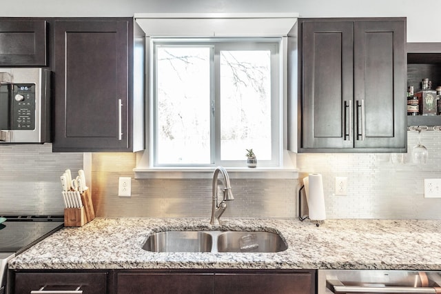 kitchen with stainless steel microwave, a sink, dark brown cabinets, and decorative backsplash