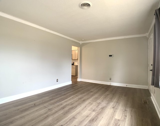 empty room featuring baseboards, crown molding, visible vents, and wood finished floors