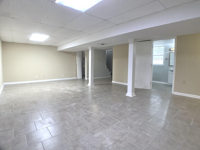 basement featuring light tile patterned flooring, a drop ceiling, baseboards, and stairs