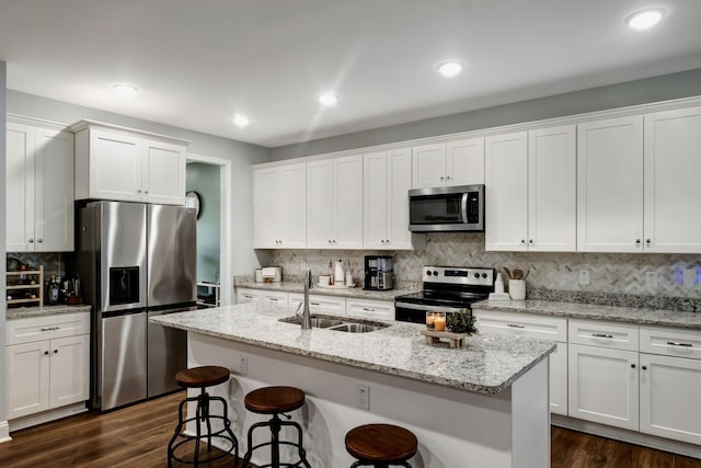 kitchen featuring a center island with sink, white cabinets, light stone counters, appliances with stainless steel finishes, and a sink