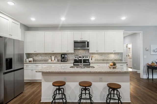 kitchen with stainless steel appliances, tasteful backsplash, an island with sink, and white cabinetry