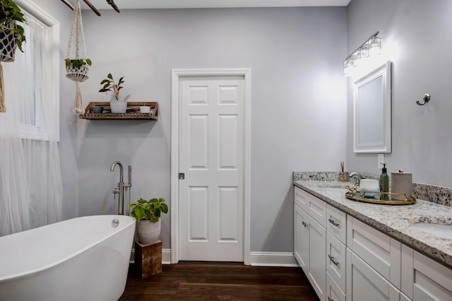 bathroom with double vanity, baseboards, wood finished floors, a freestanding tub, and a sink