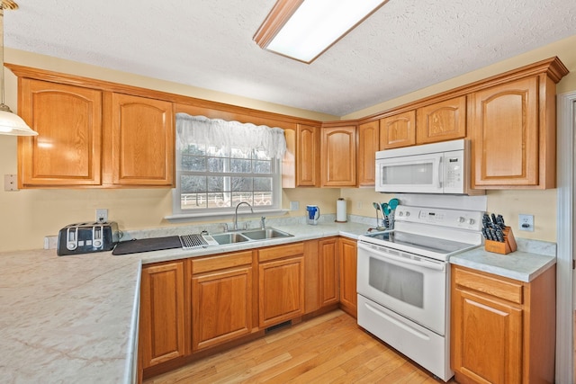 kitchen with white appliances, brown cabinetry, light countertops, light wood-type flooring, and a sink