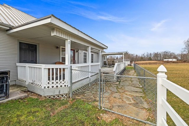 view of property exterior featuring covered porch, metal roof, a yard, and fence private yard