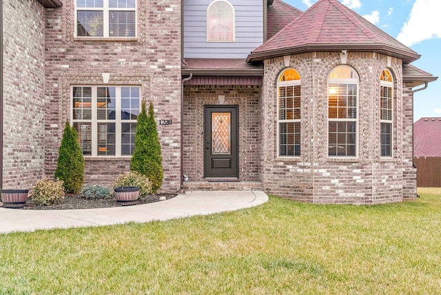 property entrance with a yard, brick siding, and a shingled roof