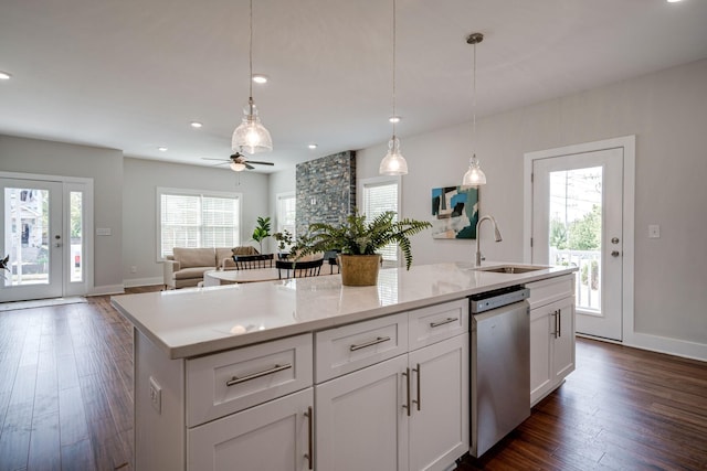 kitchen featuring a kitchen island with sink, a sink, open floor plan, stainless steel dishwasher, and decorative light fixtures