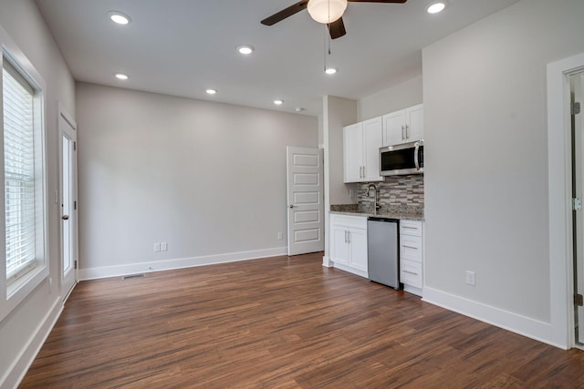 kitchen featuring light stone counters, stainless steel appliances, dark wood-type flooring, white cabinets, and decorative backsplash