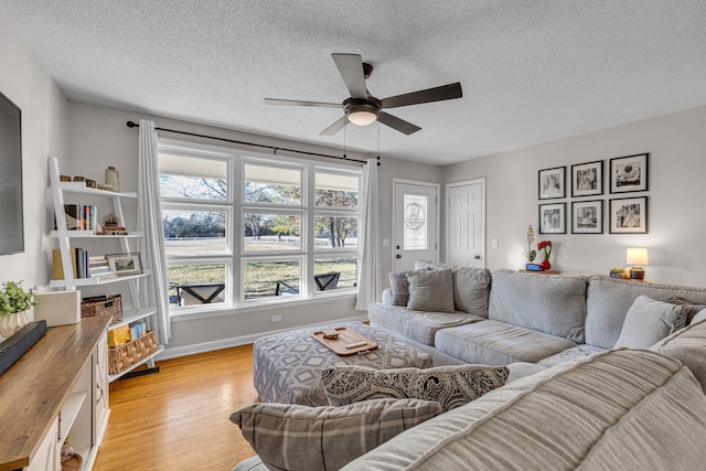 living room featuring baseboards, a textured ceiling, a ceiling fan, and light wood-style floors