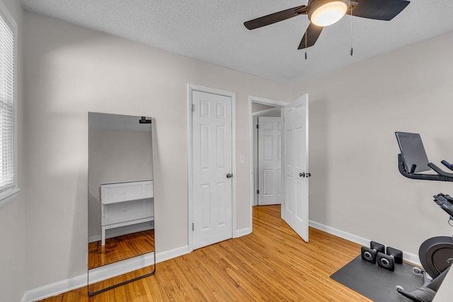 workout area with a ceiling fan, a textured ceiling, baseboards, and wood finished floors