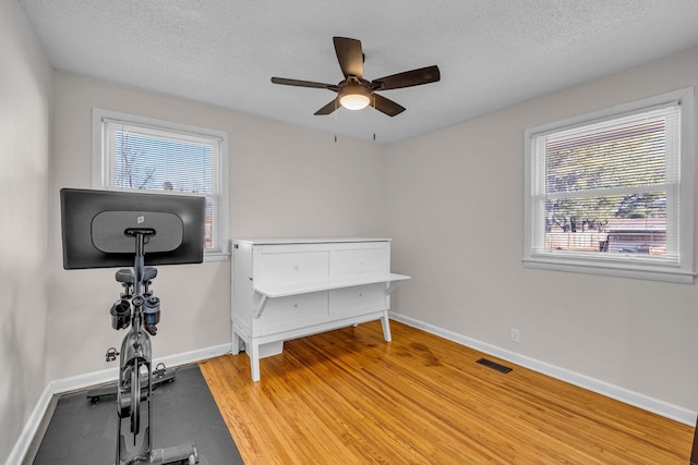 interior space featuring visible vents, a textured ceiling, baseboards, and wood finished floors