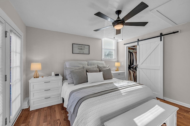 bedroom with a barn door, dark wood-style flooring, baseboards, a spacious closet, and a closet