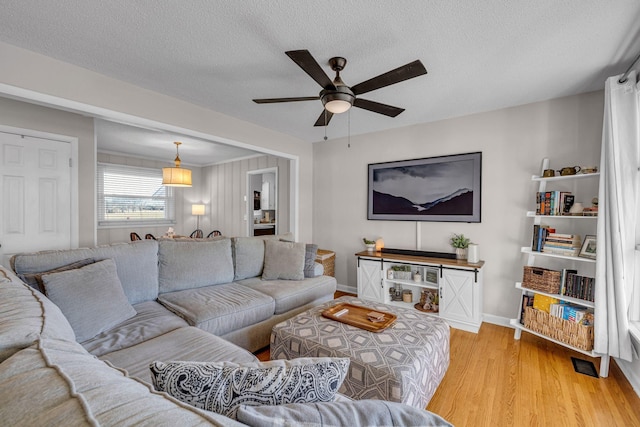 living room featuring a ceiling fan, light wood-style flooring, baseboards, and a textured ceiling