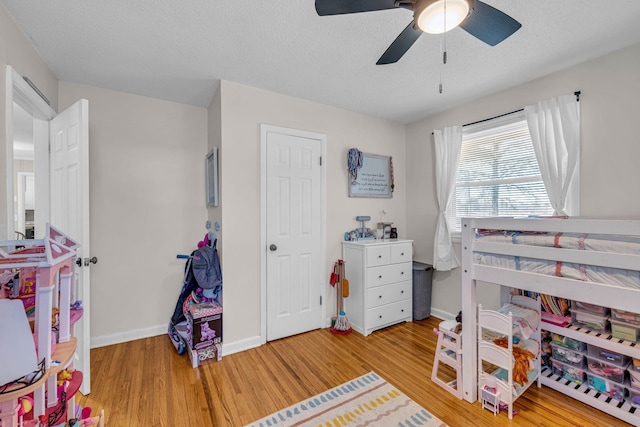 bedroom with light wood-type flooring, ceiling fan, a textured ceiling, and baseboards