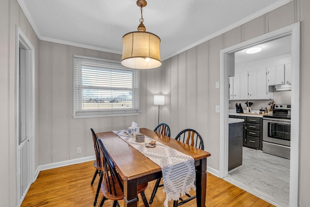 dining area with baseboards, ornamental molding, light wood-style flooring, and a decorative wall