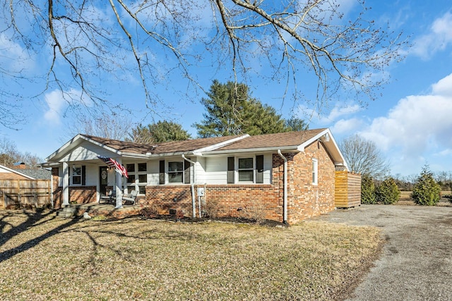 ranch-style house with covered porch, brick siding, a front yard, and fence