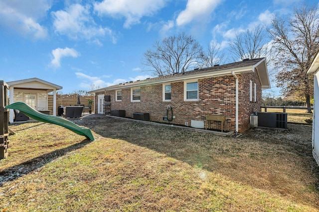 back of property with central AC unit, a playground, brick siding, fence, and a yard