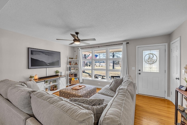 living room featuring light wood-style floors, a textured ceiling, baseboards, and a ceiling fan