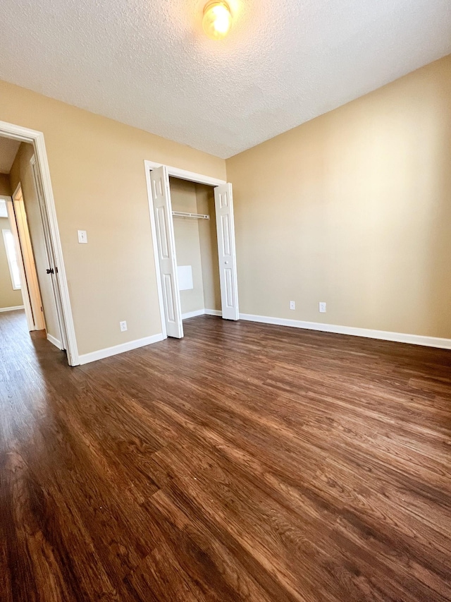 unfurnished bedroom with a closet, dark wood-style flooring, a textured ceiling, and baseboards