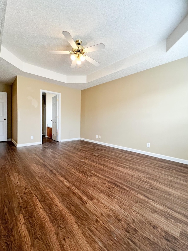 spare room with a textured ceiling, ceiling fan, dark wood-type flooring, and a raised ceiling