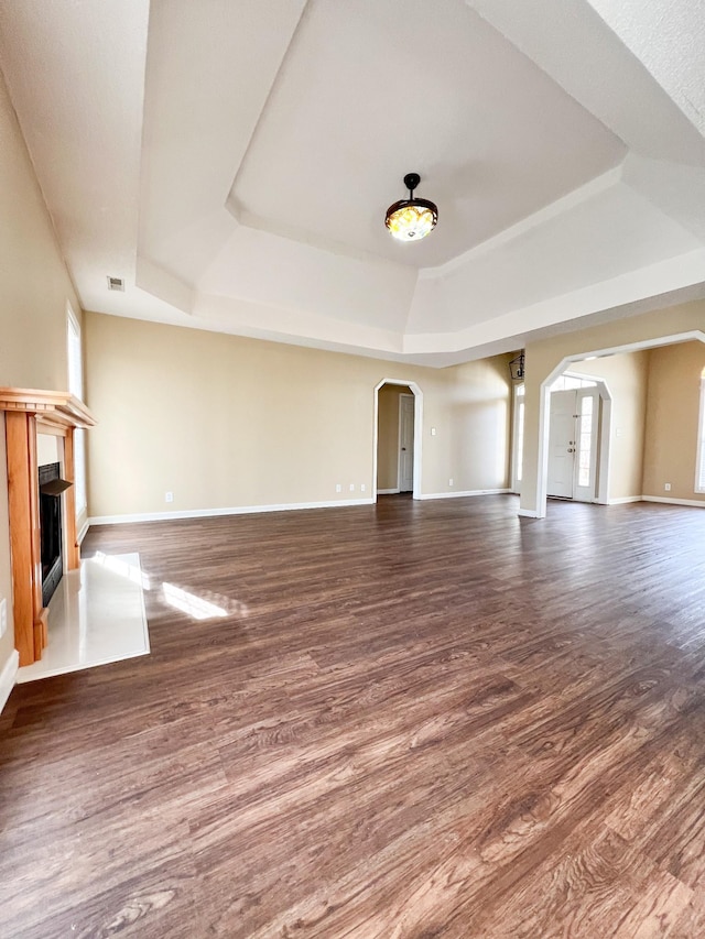 unfurnished living room with arched walkways, a raised ceiling, a fireplace, and dark wood-style flooring