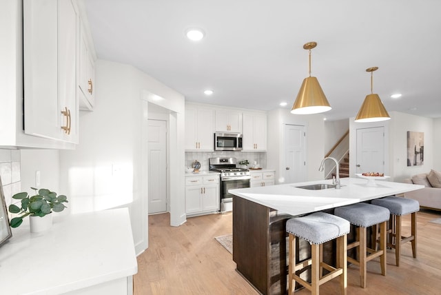 kitchen with a sink, white cabinetry, light countertops, appliances with stainless steel finishes, and decorative light fixtures