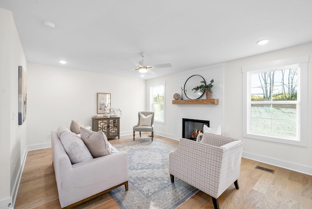 living room featuring a large fireplace, visible vents, light wood-style flooring, and baseboards