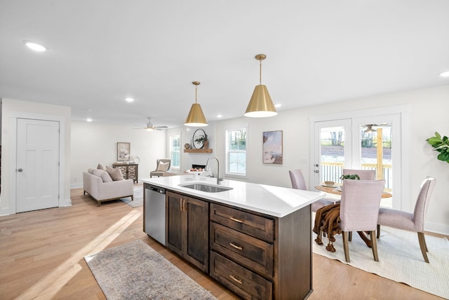 kitchen featuring dishwasher, a kitchen island with sink, light countertops, pendant lighting, and a sink