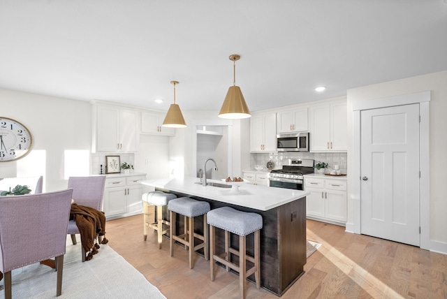 kitchen with decorative light fixtures, light countertops, appliances with stainless steel finishes, white cabinetry, and an island with sink