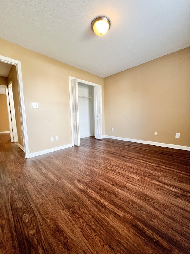 unfurnished bedroom with baseboards, dark wood finished floors, and a closet