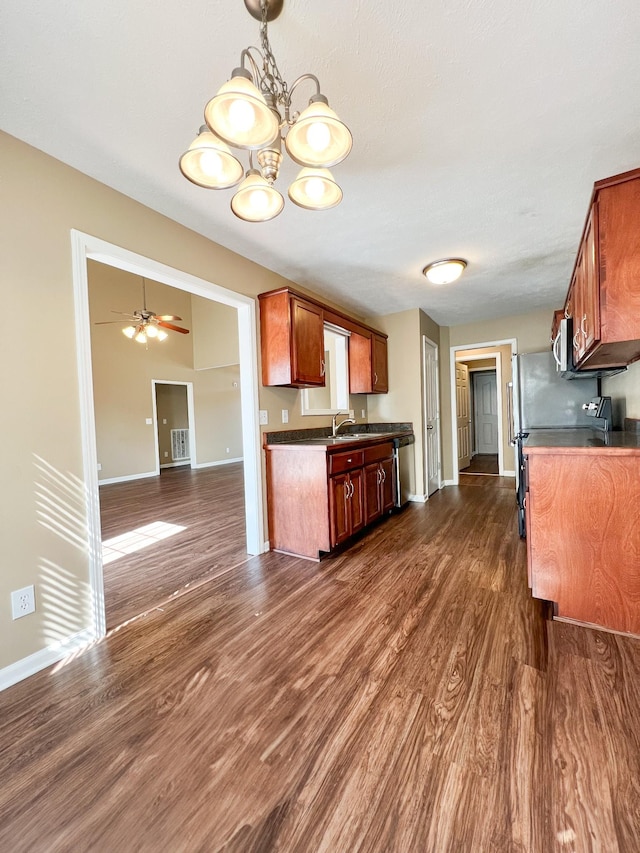 kitchen with dark countertops, stainless steel microwave, dark wood-style flooring, a sink, and ceiling fan with notable chandelier