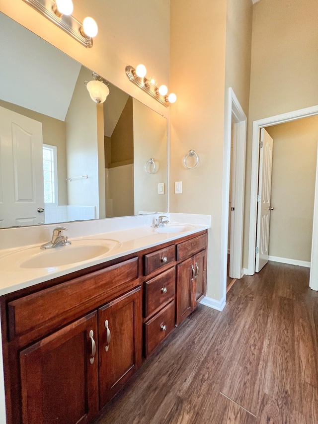 full bathroom with lofted ceiling, wood finished floors, a sink, and double vanity