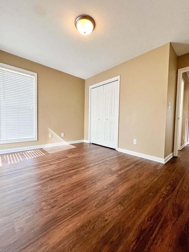 unfurnished bedroom with dark wood-style floors, a closet, and baseboards