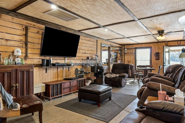 living area featuring finished concrete floors, visible vents, wooden walls, and a ceiling fan
