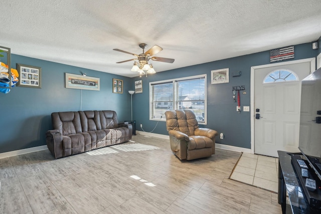 living area with a ceiling fan, a textured ceiling, and baseboards