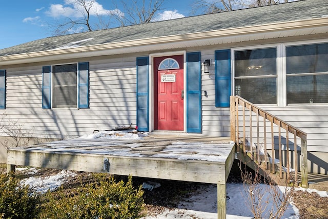 snow covered property entrance with roof with shingles and a deck