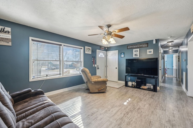 living room with light wood finished floors, ceiling fan, baseboards, and a textured ceiling