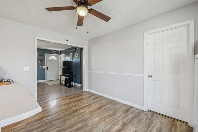 empty room with ceiling fan, a textured ceiling, baseboards, and wood finished floors